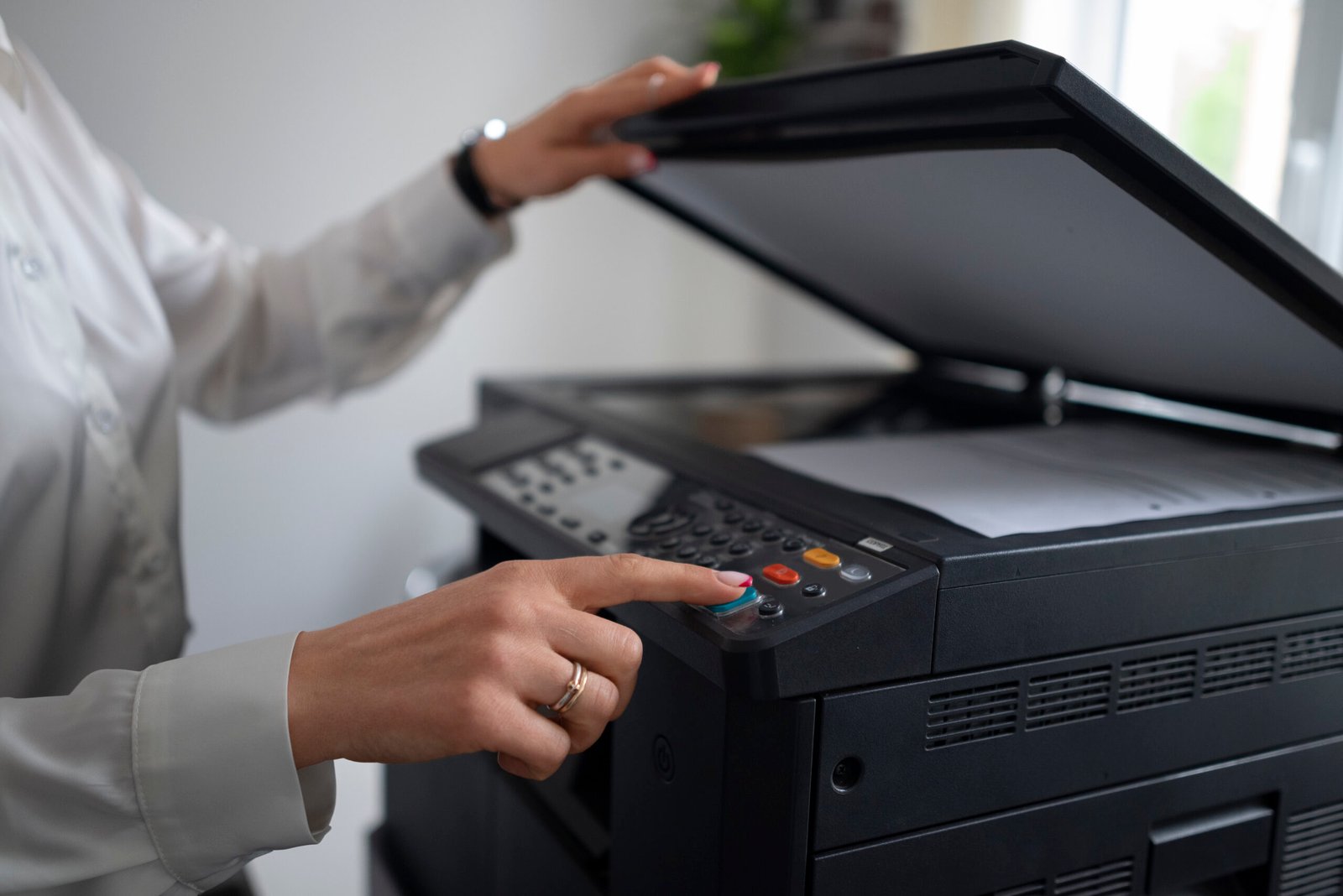 Person operating a copier, pressing the control panel on a multifunction printer.